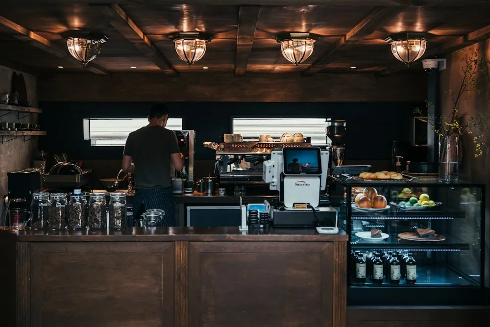 Barista za drewnianą ladą kawiarni z witryną pełną wypieków